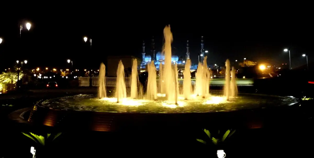 View towards the lit mosque at night past a fountain